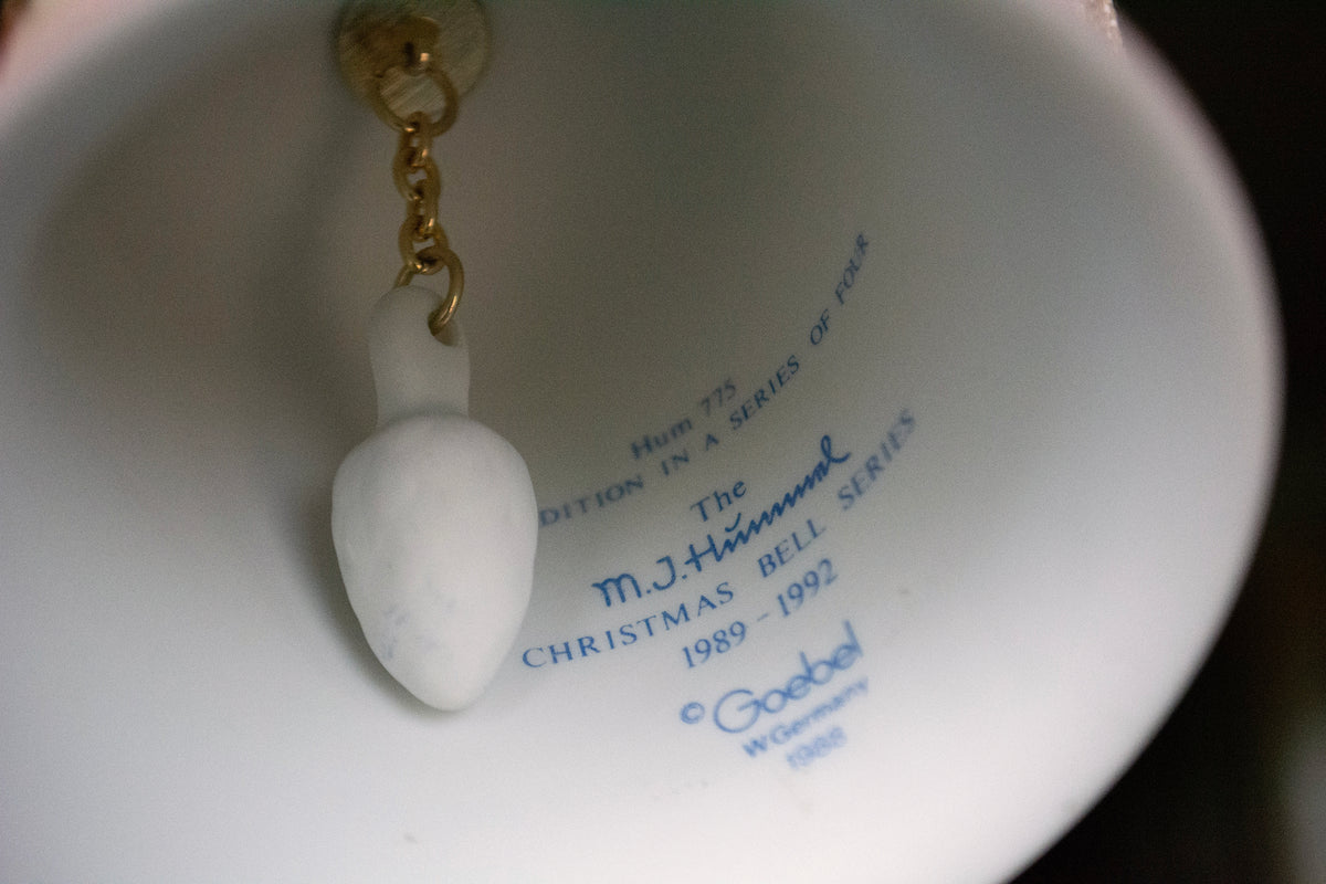 Close-up of the inside of a white ceramic Christmas bell with blue printed text and a small white hanging ornament attached by a gold chain.