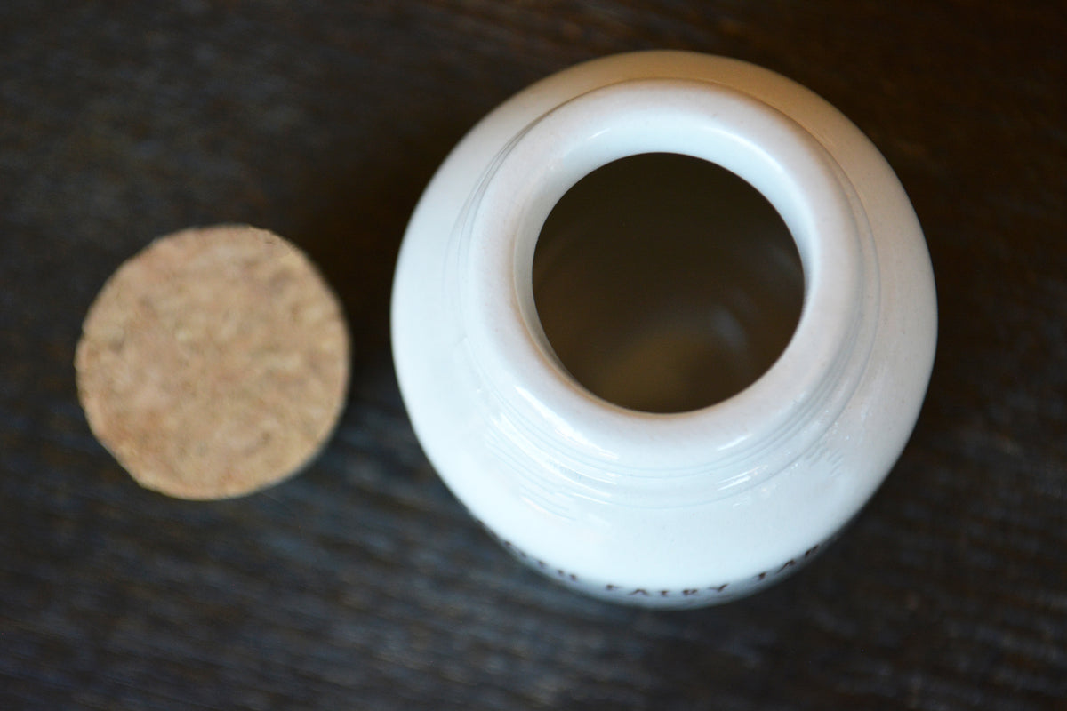 A white ceramic jar with its cork lid resting beside it on a dark wooden surface.